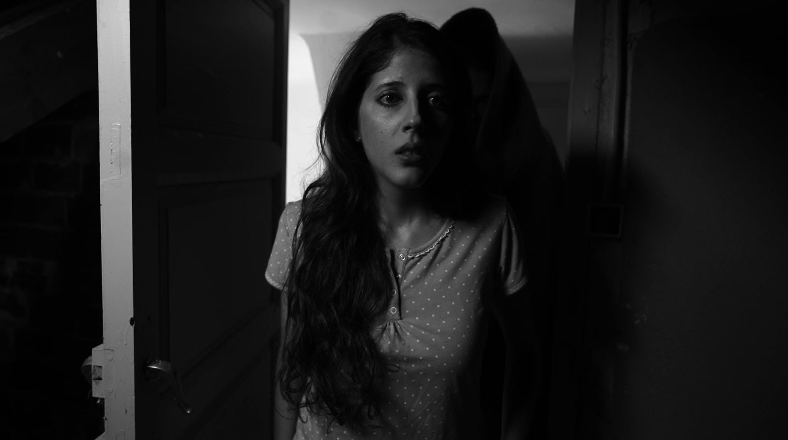 Mujer en un pasillo oscuro en una escena de suspense en blanco y negro